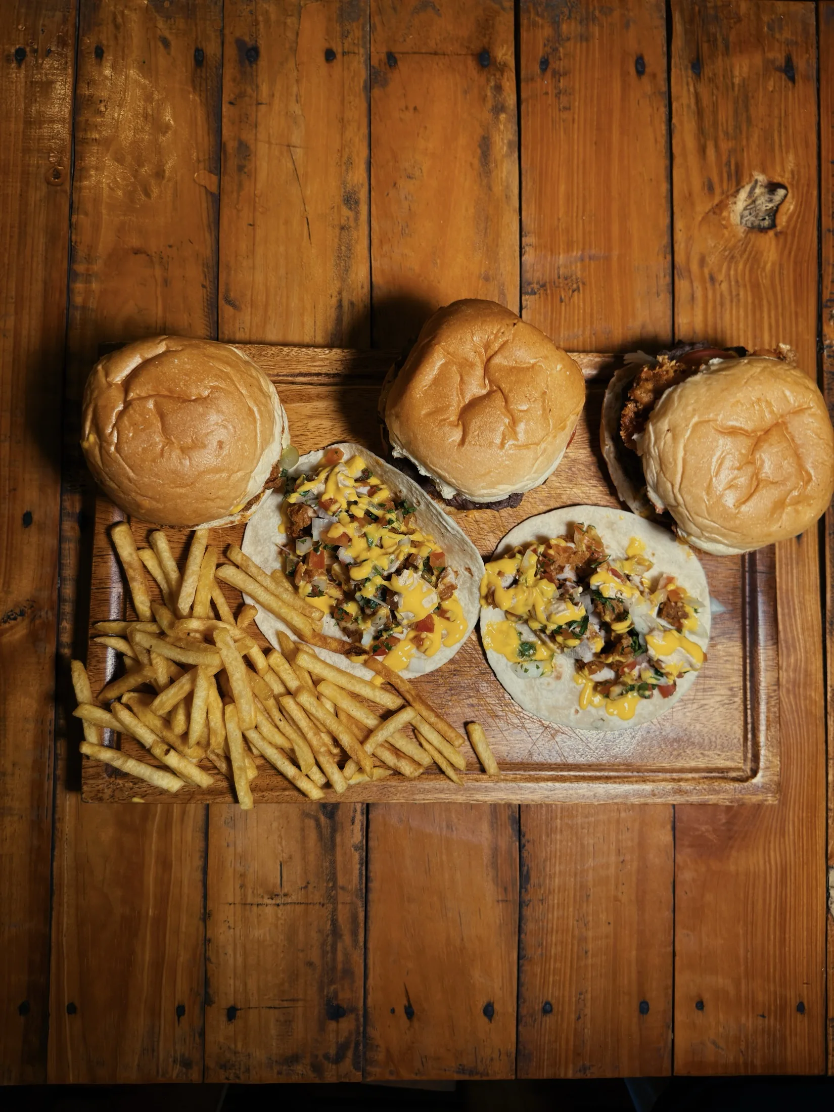 Overhead view of burgers, tacos and fries on a wooden board