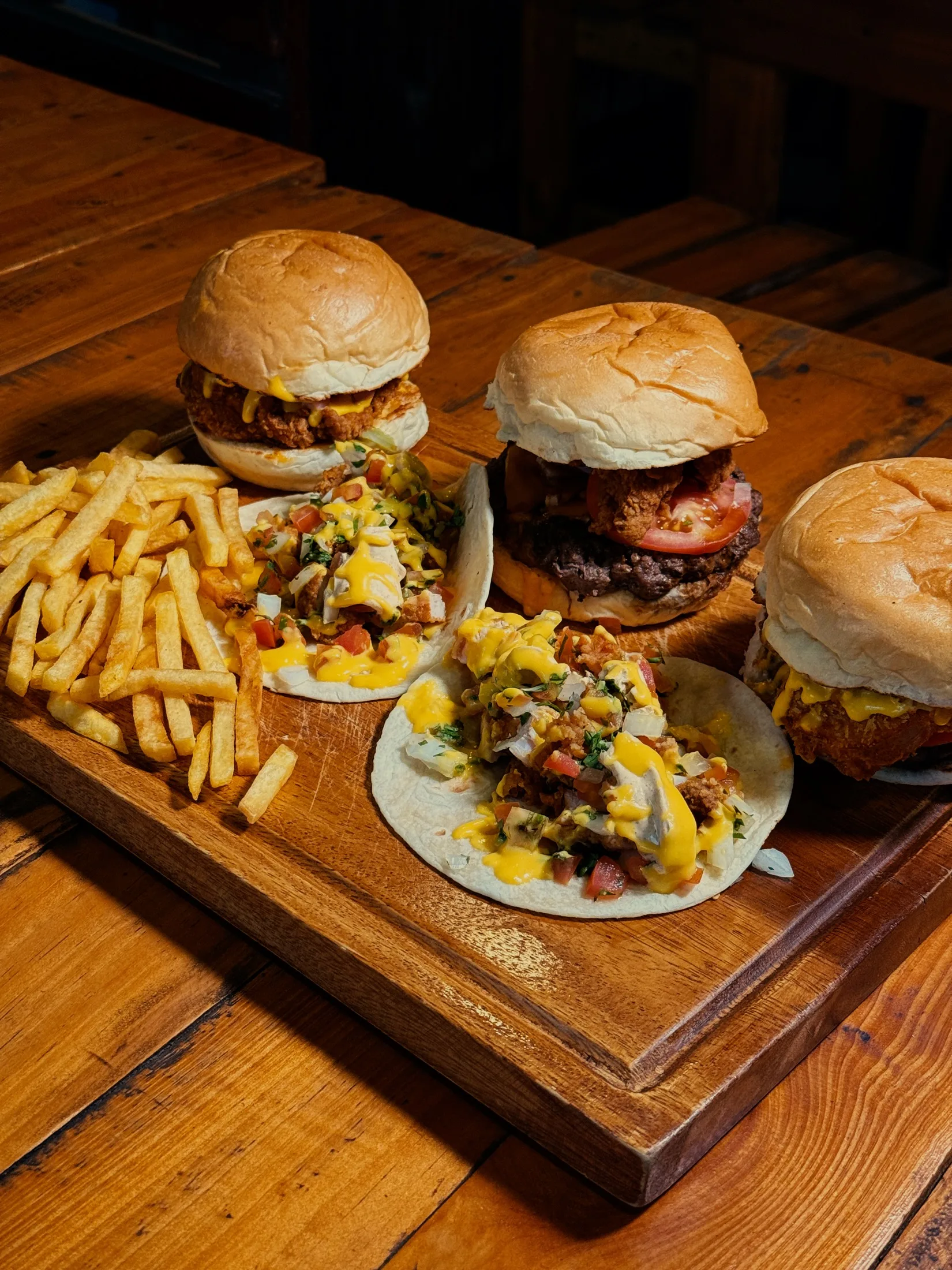 Burgers, tacos and fries arranged on a wooden board