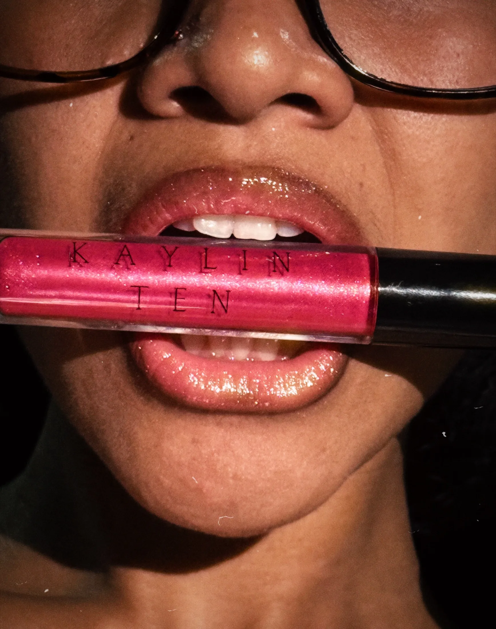 Close-up of a pink lip gloss held in front of a smiling face