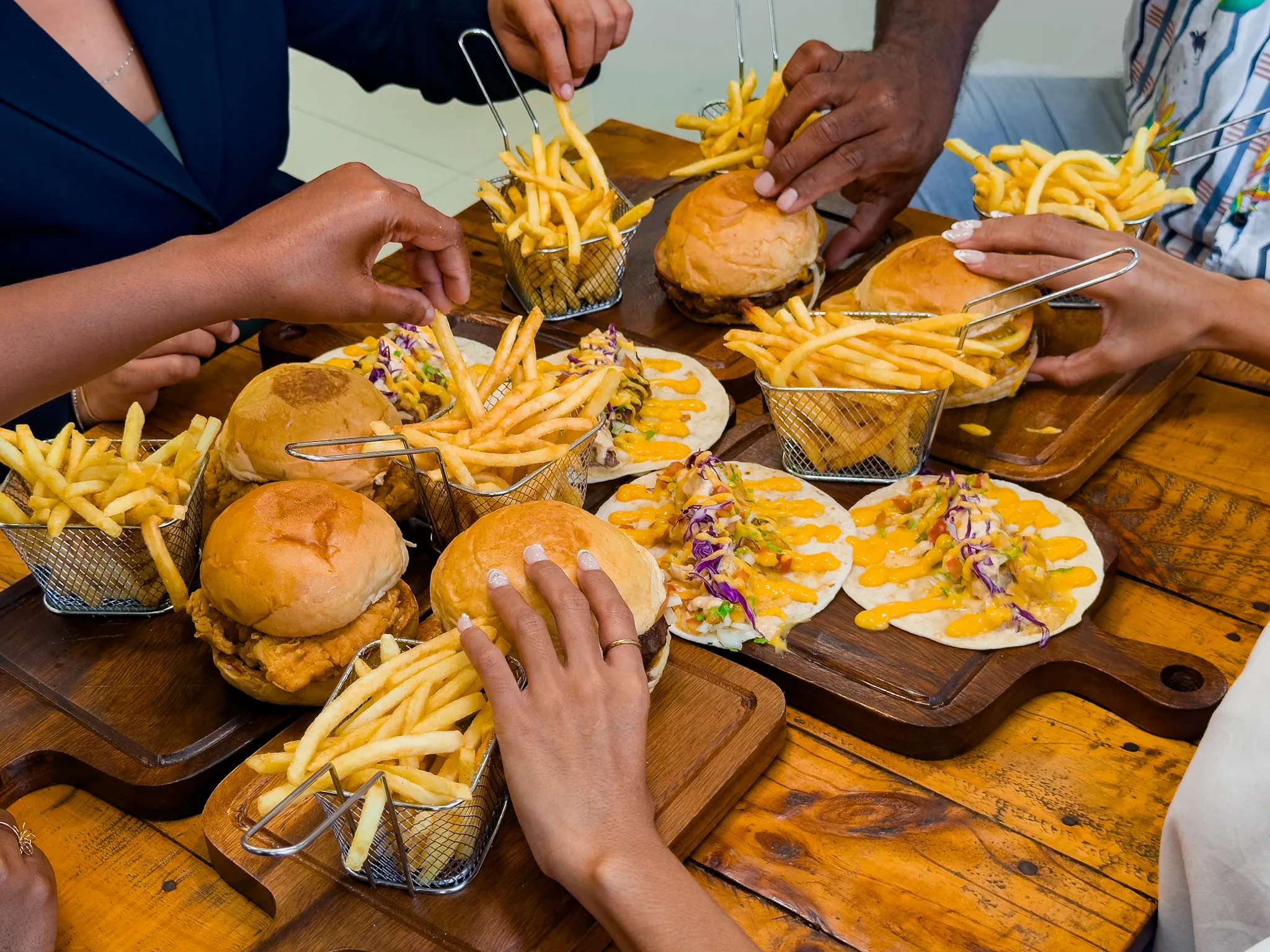 People reaching for burgers, tacos and fries at a table